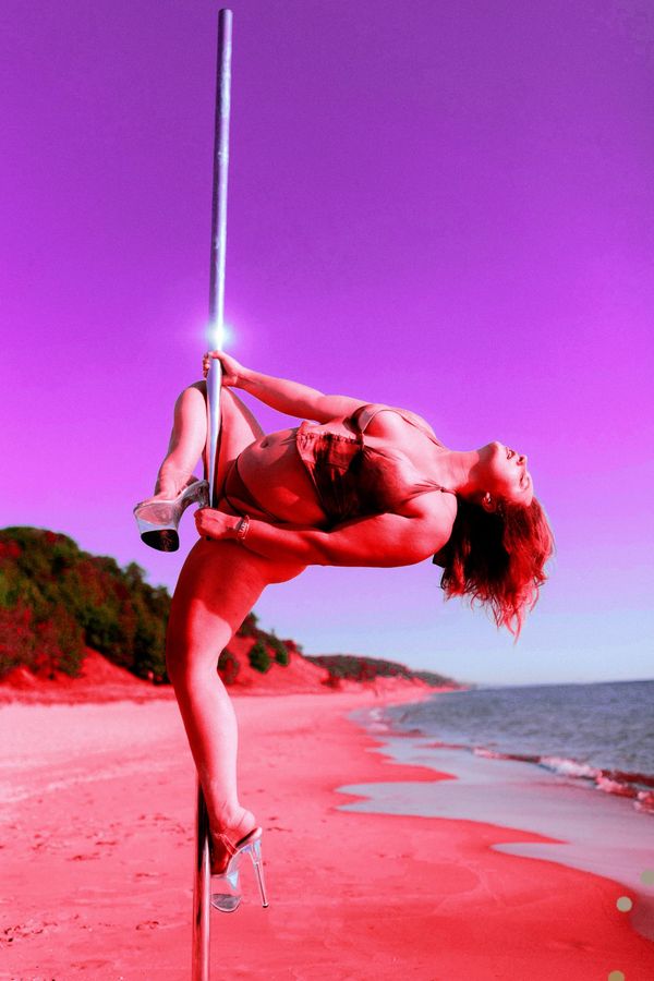 A pole dancer in a layback on the pole, violet sky and red sand behind her